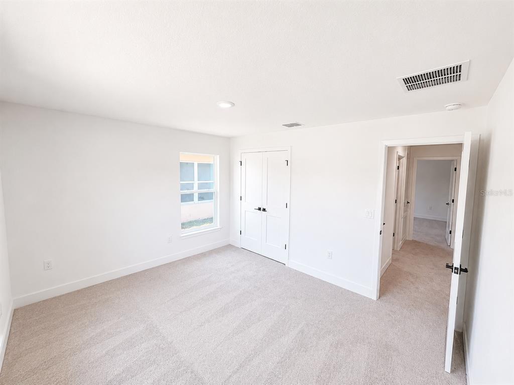 A bedroom with white walls, beige carpet, a window, and a double-door closet — 7636 BENT TREE LOOP, ST CLOUD, FL