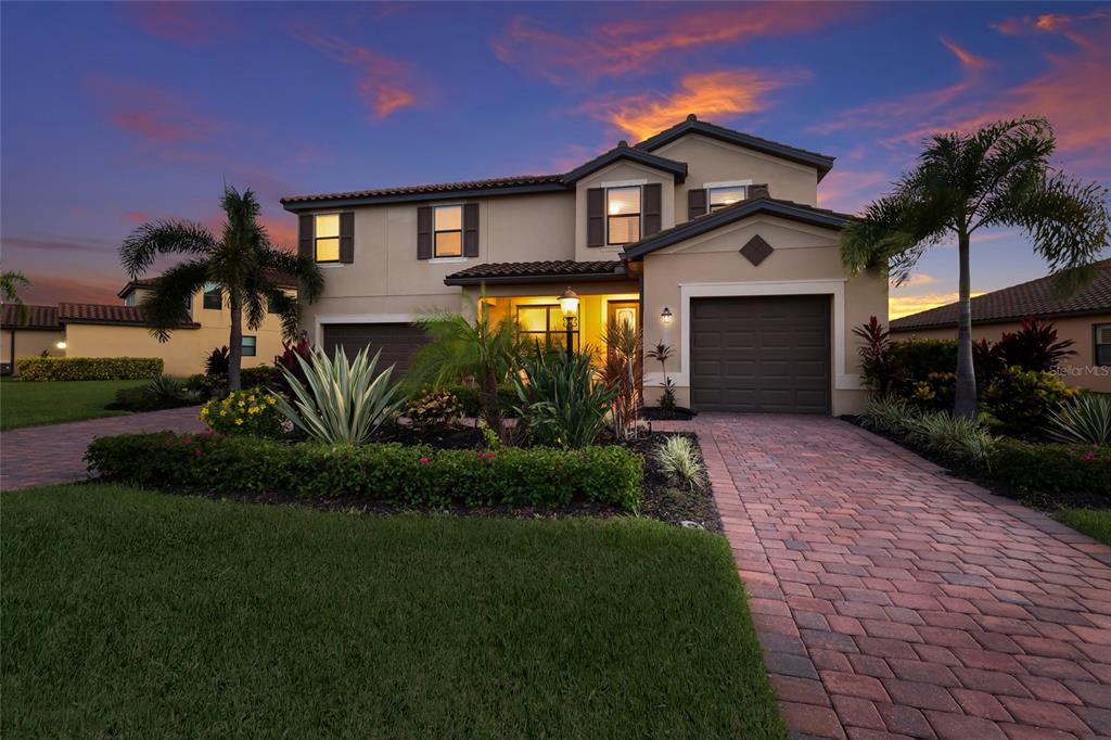 A two-story suburban house with a paved driveway, palm trees, and a sunset sky — 3618 SCRUB CREEK RUN, LAKEWOOD RANCH, FL