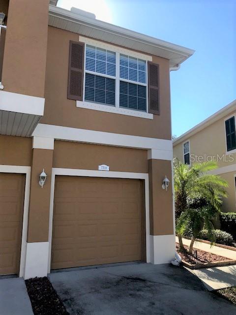A two-story tan townhouse exterior features a single-car garage and a second-story window with shutters — 7708 RED MILL CIRCLE, NEW PORT RICHEY, FL