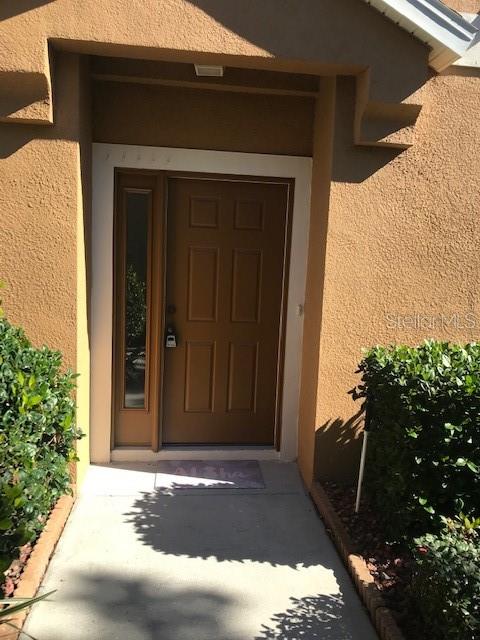 A brown front door with a side window is set within a tan stucco entryway — 7708 RED MILL CIRCLE, NEW PORT RICHEY, FL