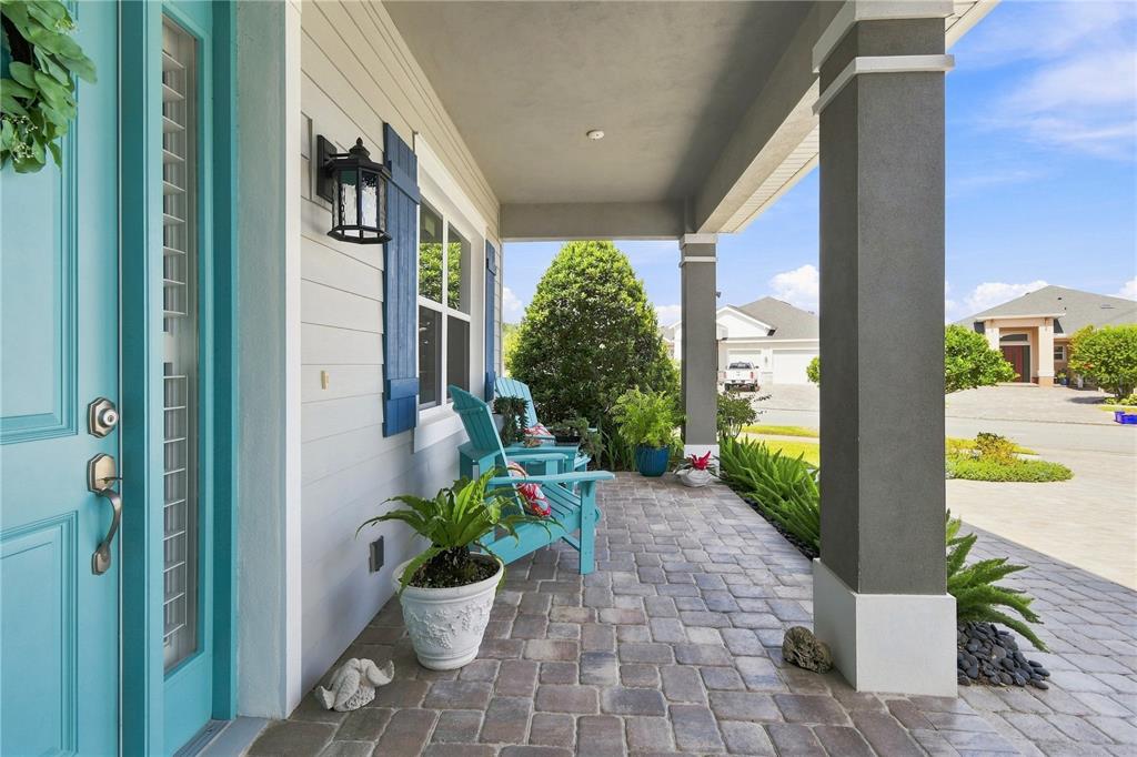 A covered front porch features a teal door, two blue chairs, and stone paver flooring — 2811 SIENNA VIEW TERRACE COURT, NEW SMYRNA BEACH, FL