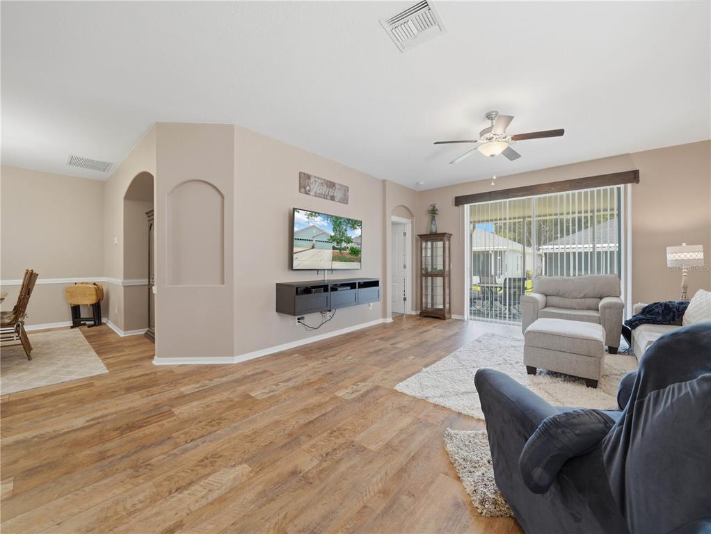 A living room features wood-look flooring, a wall-mounted television, and a sliding glass door — 6936 SURREY OAK DRIVE, APOLLO BEACH, FL