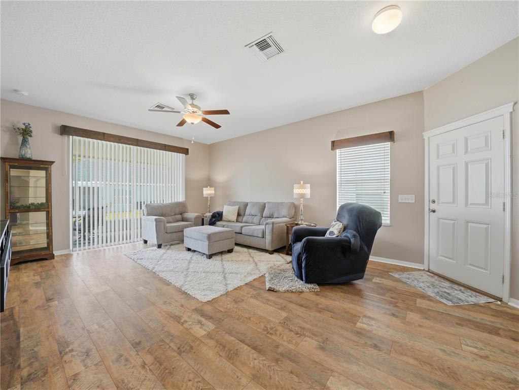 A living room features wood-look flooring, a ceiling fan, a sofa set, and a front door — 6936 SURREY OAK DRIVE, APOLLO BEACH, FL