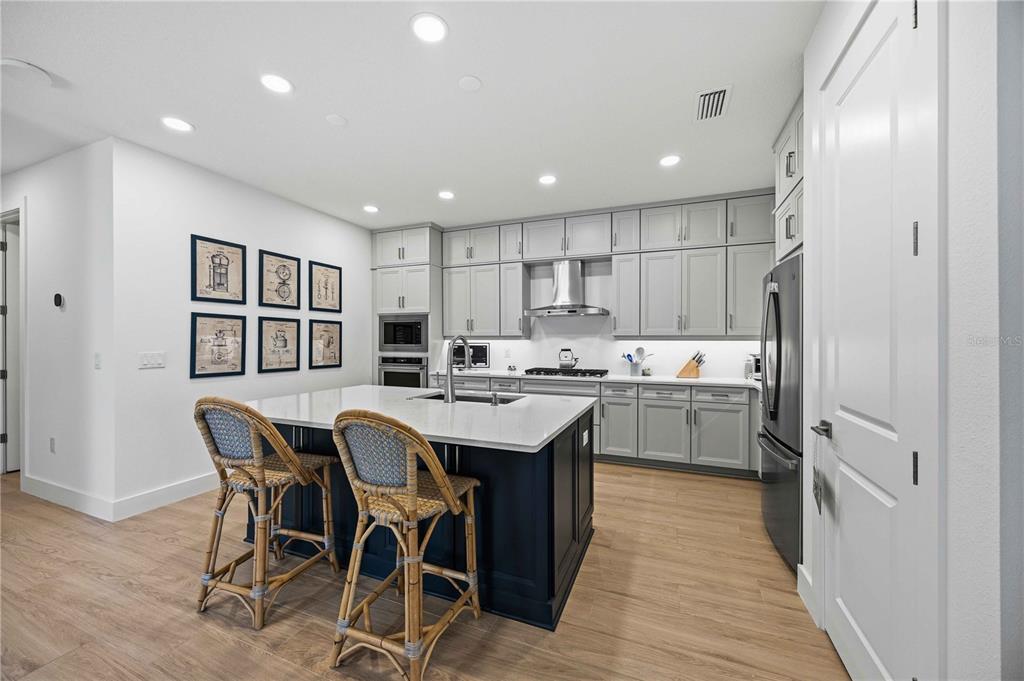 A kitchen features a dark blue island with bar stools, gray cabinetry, and light flooring — 18652 DAYSPRING PLACE, VENICE, FL