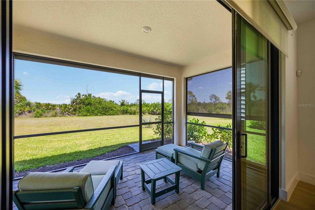 A screened-in patio with brick pavers overlooks a grassy field and natural landscape — 18652 DAYSPRING PLACE, VENICE, FL