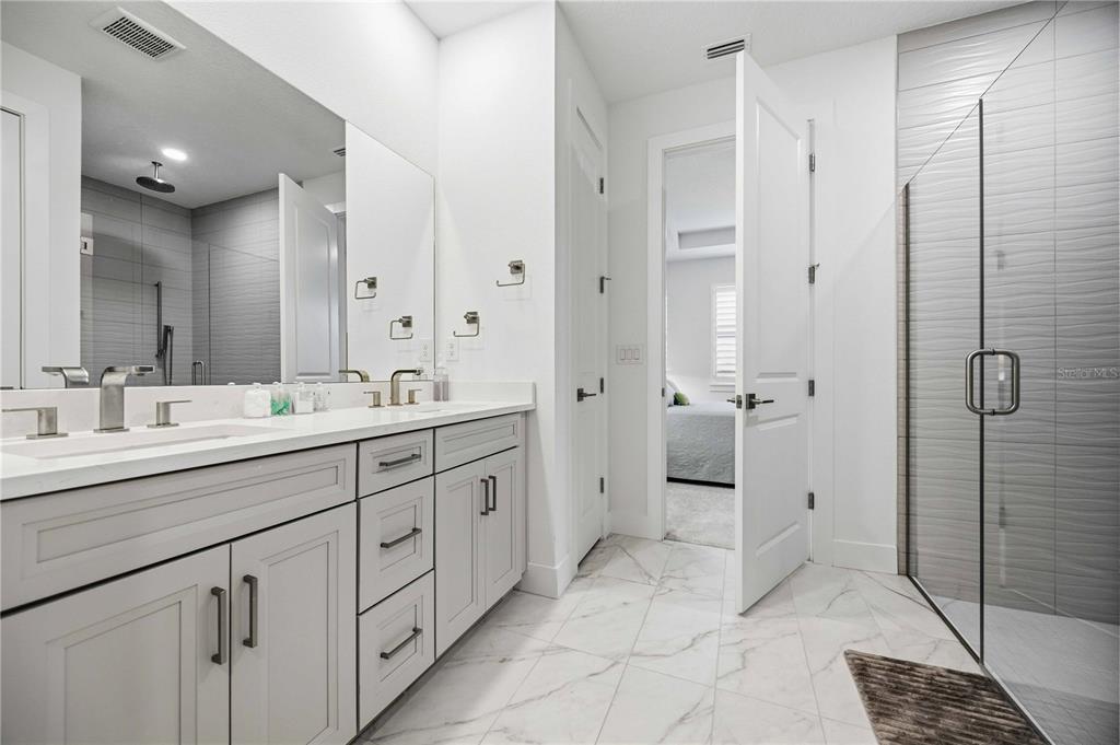 A modern bathroom features a double vanity, a glass-enclosed shower, and white marble-style flooring — 18652 DAYSPRING PLACE, VENICE, FL