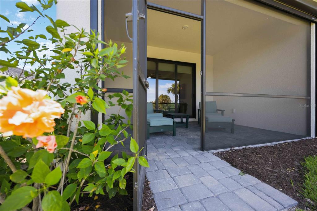 A paved walkway leads through a screen door to a covered patio with lounge chairs — 18652 DAYSPRING PLACE, VENICE, FL