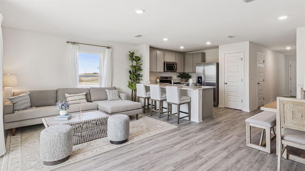 An open-concept living room and kitchen feature gray cabinetry, stainless appliances, and wood-look flooring — 2334 AVEENO AVENUE, HAINES CITY, FL