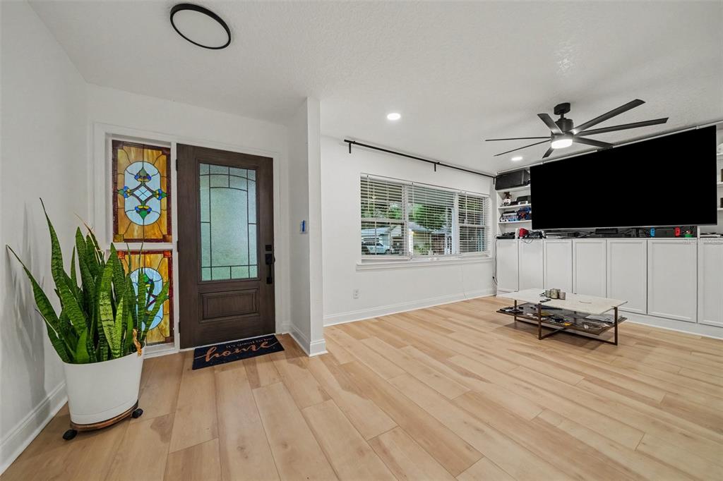 A living room features light wood flooring, white walls, a stained-glass window, and built-in cabinetry — 1905 BONANZA CT, WINTER PARK, FL