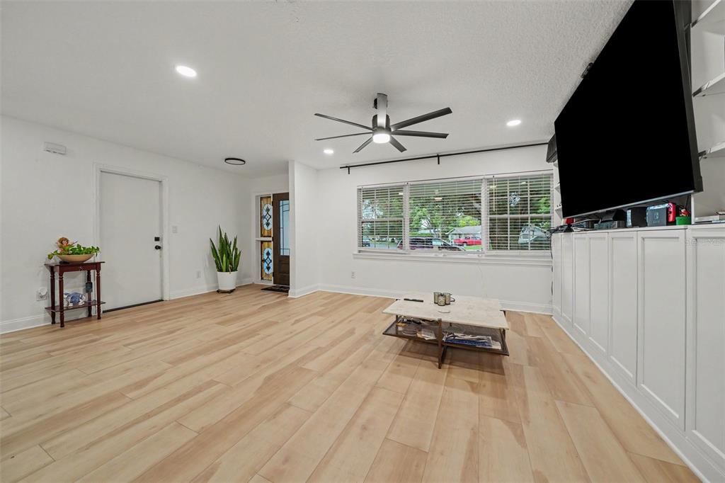 A living room features light wood-look flooring, white built-in cabinetry, and a large wall-mounted television — 1905 BONANZA CT, WINTER PARK, FL