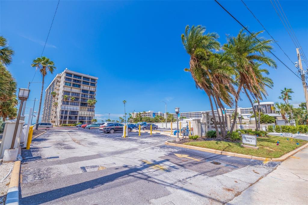 An outdoor parking lot leads to a tall residential building under a clear blue sky — 5396 GULF BOULEVARD UNIT 209, ST PETE BEACH, FL