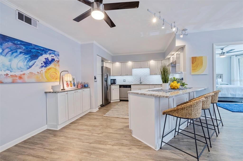 A bright kitchen features white cabinetry, granite countertops, a central island, and wood-look flooring — 5396 GULF BOULEVARD UNIT 209, ST PETE BEACH, FL