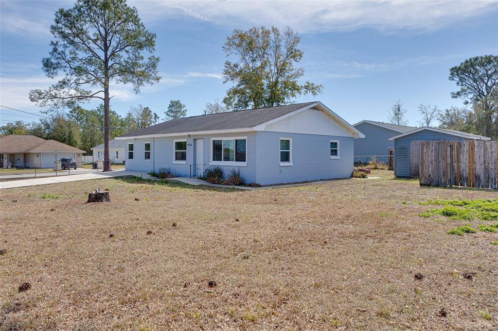A light blue single-story house with a white roof and a detached shed in the yard — 9782 SE 157TH LANE, SUMMERFIELD, FL