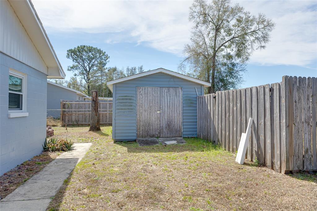 A backyard features a blue storage shed, a wooden privacy fence, and a concrete walkway — 9782 SE 157TH LANE, SUMMERFIELD, FL