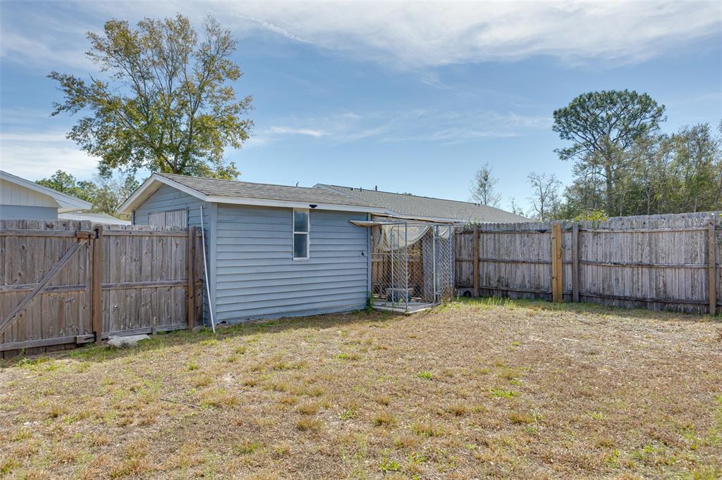 A blue house exterior with a fenced backyard and a chain-link dog kennel — 9782 SE 157TH LANE, SUMMERFIELD, FL
