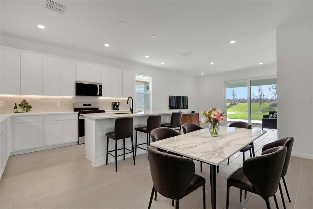 A modern kitchen and dining area feature white cabinetry, a marble-topped table, and sliding doors — 5461 NW CAMBERLY COURT, PORT ST LUCIE, FL