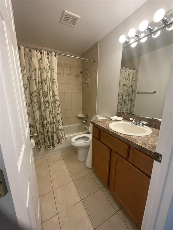 A bathroom features a tan tile shower-tub combo, a wood vanity, and a white toilet — 1440 ALBERNI STREET NW, PALM BAY, FL
