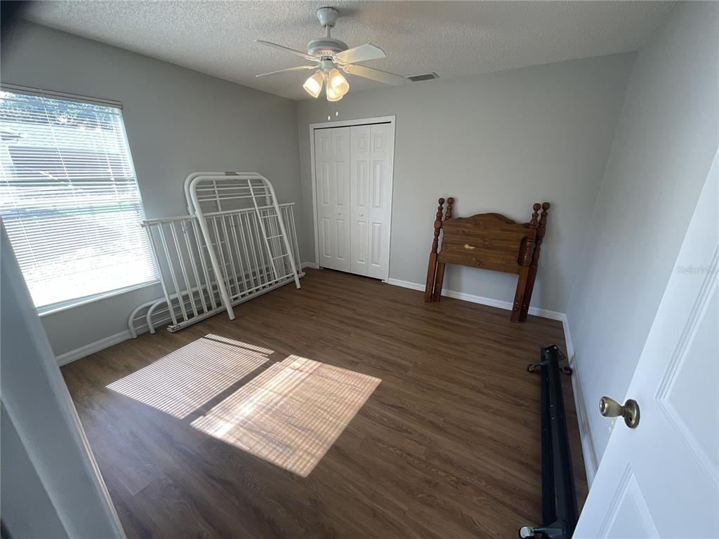 An empty bedroom features wood-look flooring, a ceiling fan, a window with blinds, and closet doors — 1440 ALBERNI STREET NW, PALM BAY, FL