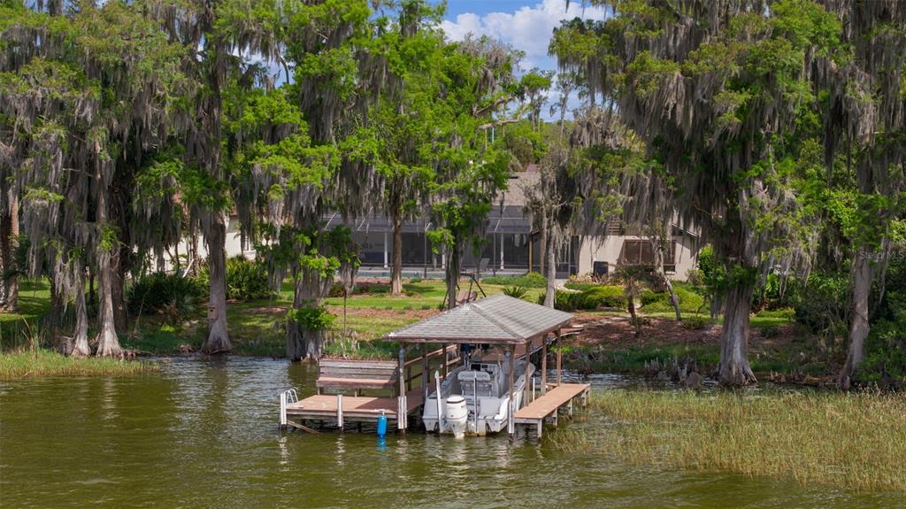 A boat dock with a covered slip sits on a lake in front of a house — 60 SAND LAKE PLACE, EUSTIS, FL