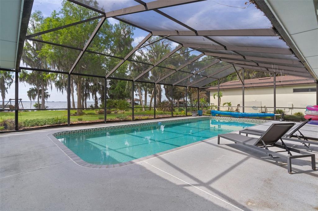 A screened-in swimming pool patio overlooks a lake with trees in the background — 60 SAND LAKE PLACE, EUSTIS, FL