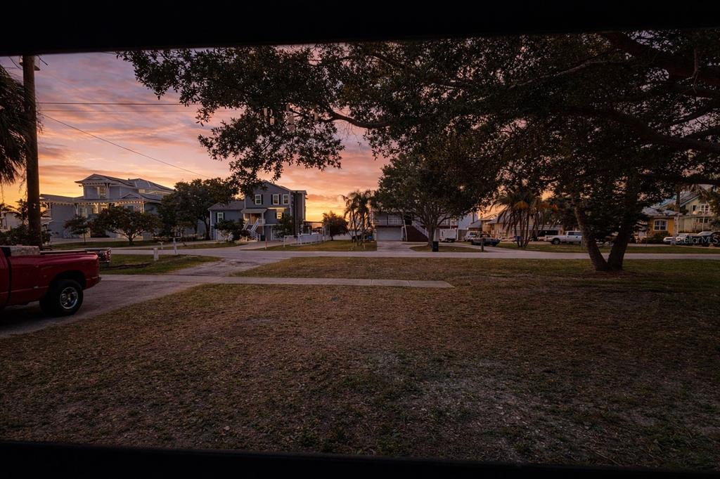 A view from a window shows a grassy yard and houses at sunset — 343 SHORE DRIVE E, OLDSMAR, FL