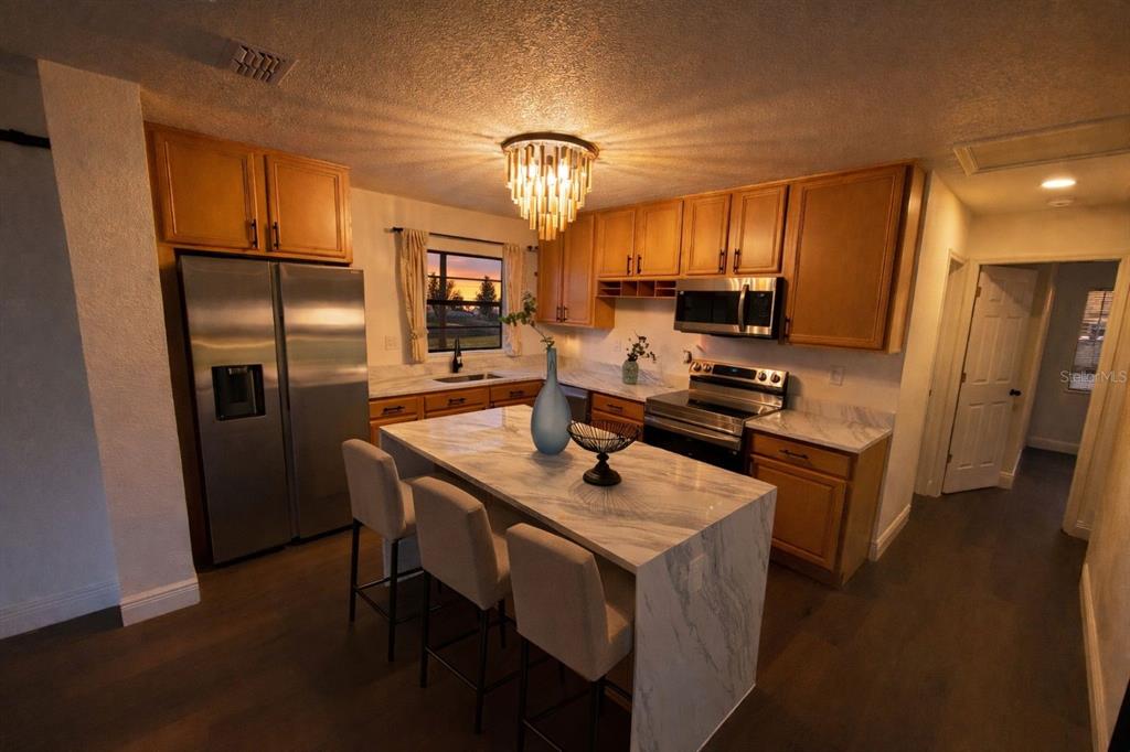 A kitchen features wood cabinets, a marble-topped island with seating, and stainless steel appliances — 343 SHORE DRIVE E, OLDSMAR, FL