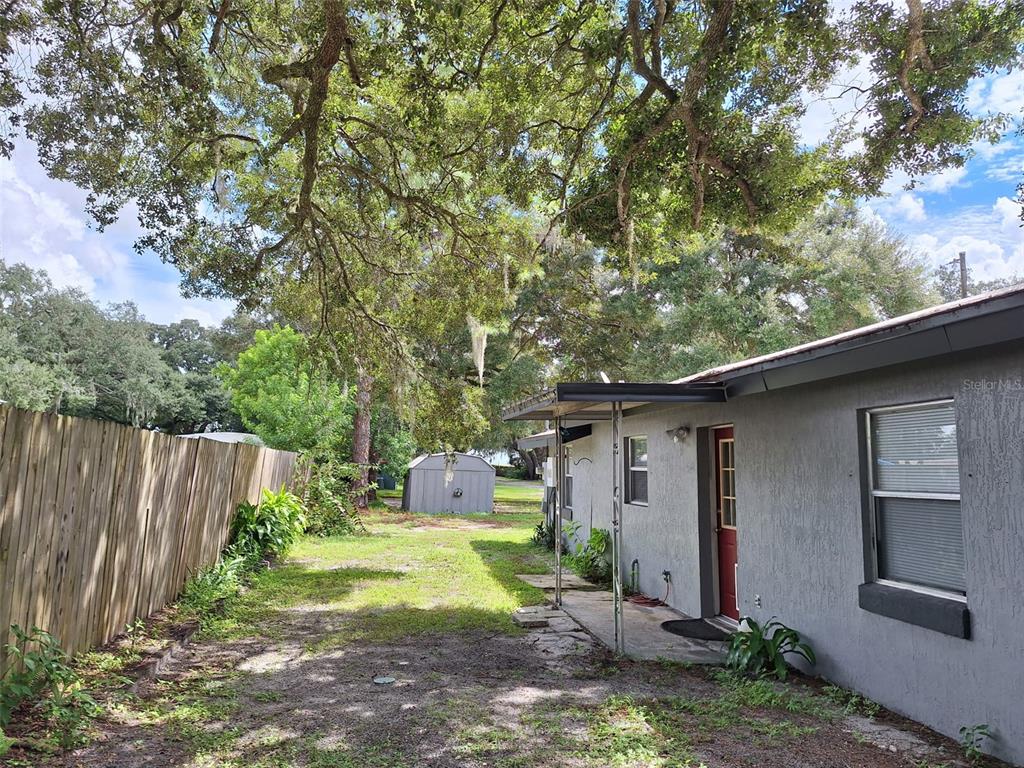 A single-story gray house with a metal shed sits on a large, tree-shaded dirt lot — 1257 LYNCHBURG ROAD, LAKE ALFRED, FL