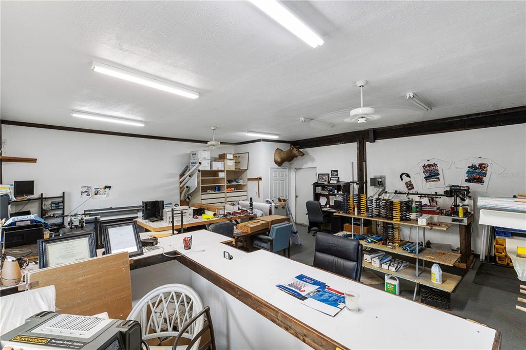 A cluttered workshop or office space features white walls, fluorescent lighting, and various workbenches — 15058 BALM ROAD, WIMAUMA, FL