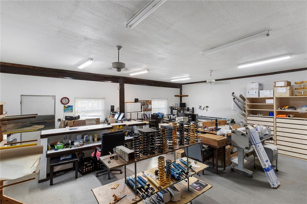 A workshop or office space features workbenches, storage shelving, and various automotive suspension components — 15058 BALM ROAD, WIMAUMA, FL