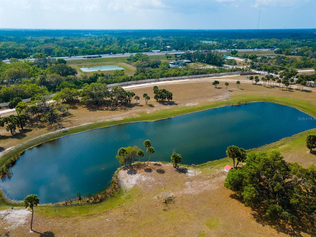 An aerial view shows a large pond surrounded by grassy land, trees, and a distant highway — 0396014400, VENICE, FL