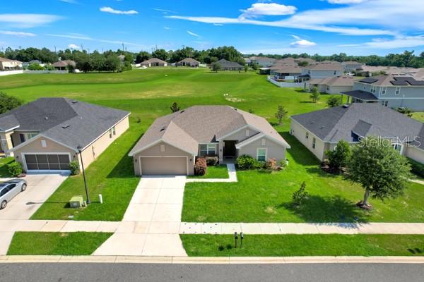 An aerial view shows three suburban houses with driveways and lawns under a blue sky — 7733 SLOEWOOD DRIVE, LEESBURG, FL
