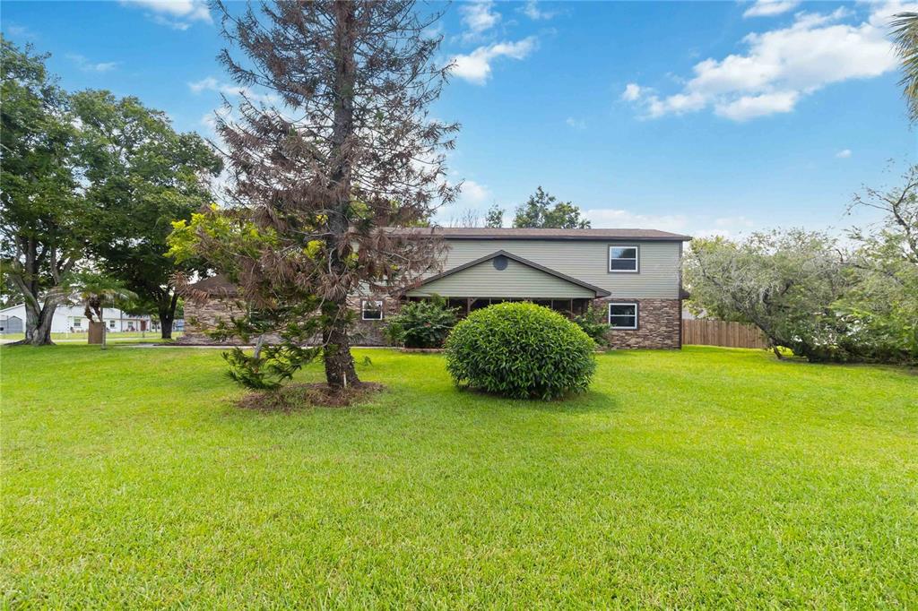 A two-story house with green siding and stone veneer sits behind a large grassy lawn — 4899 SPARROW DRIVE, ST CLOUD, FL