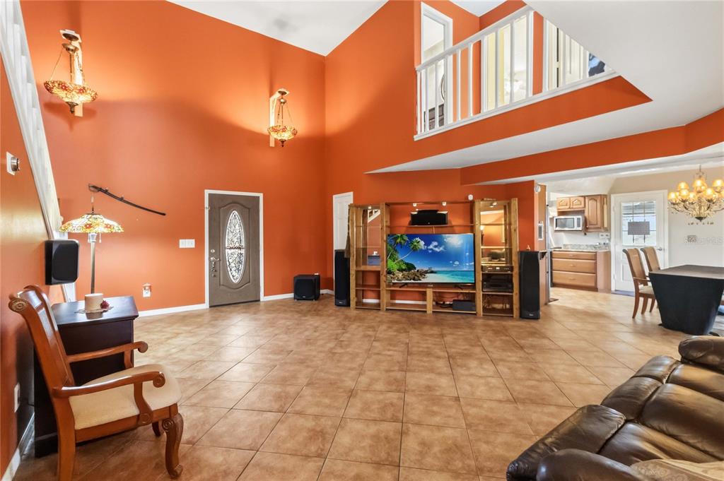 A spacious living room features orange walls, tile flooring, a high ceiling, and a loft balcony — 4899 SPARROW DRIVE, ST CLOUD, FL