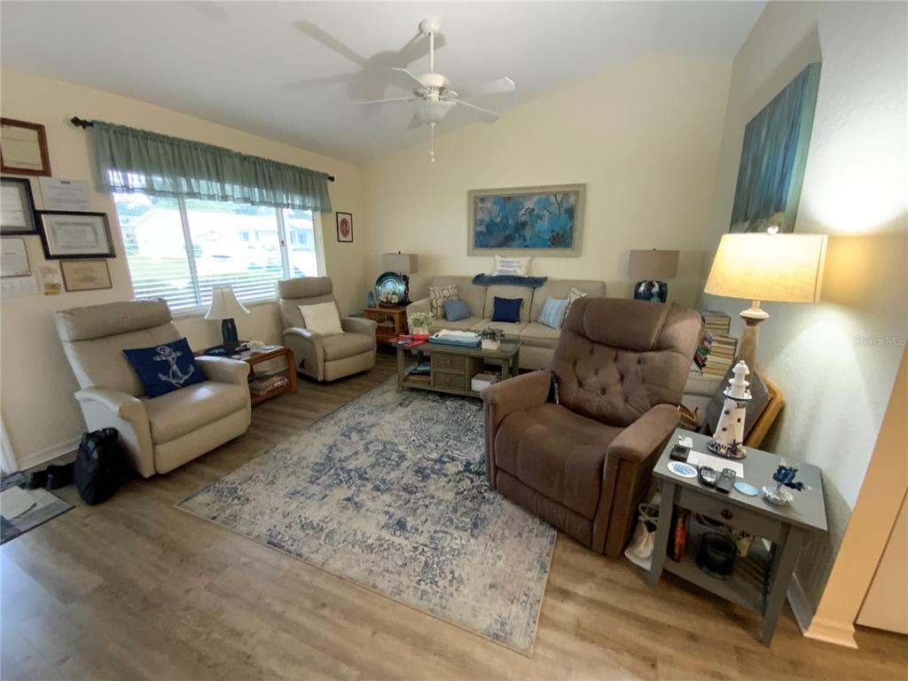A living room features light-colored walls, wood-look flooring, a ceiling fan, and several seating pieces — 9486 SE 173RD PLACE, SUMMERFIELD, FL