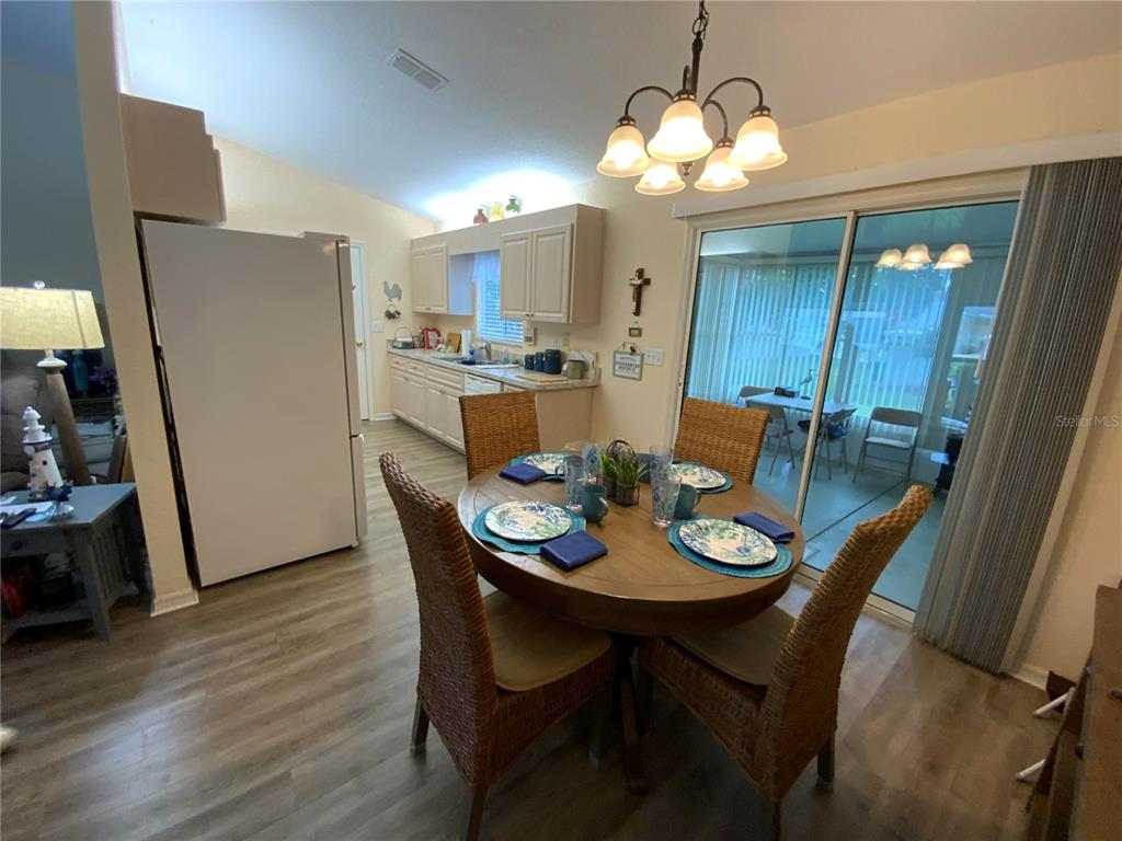 A dining area with a round wooden table and wicker chairs sits beside a kitchen — 9486 SE 173RD PLACE, SUMMERFIELD, FL