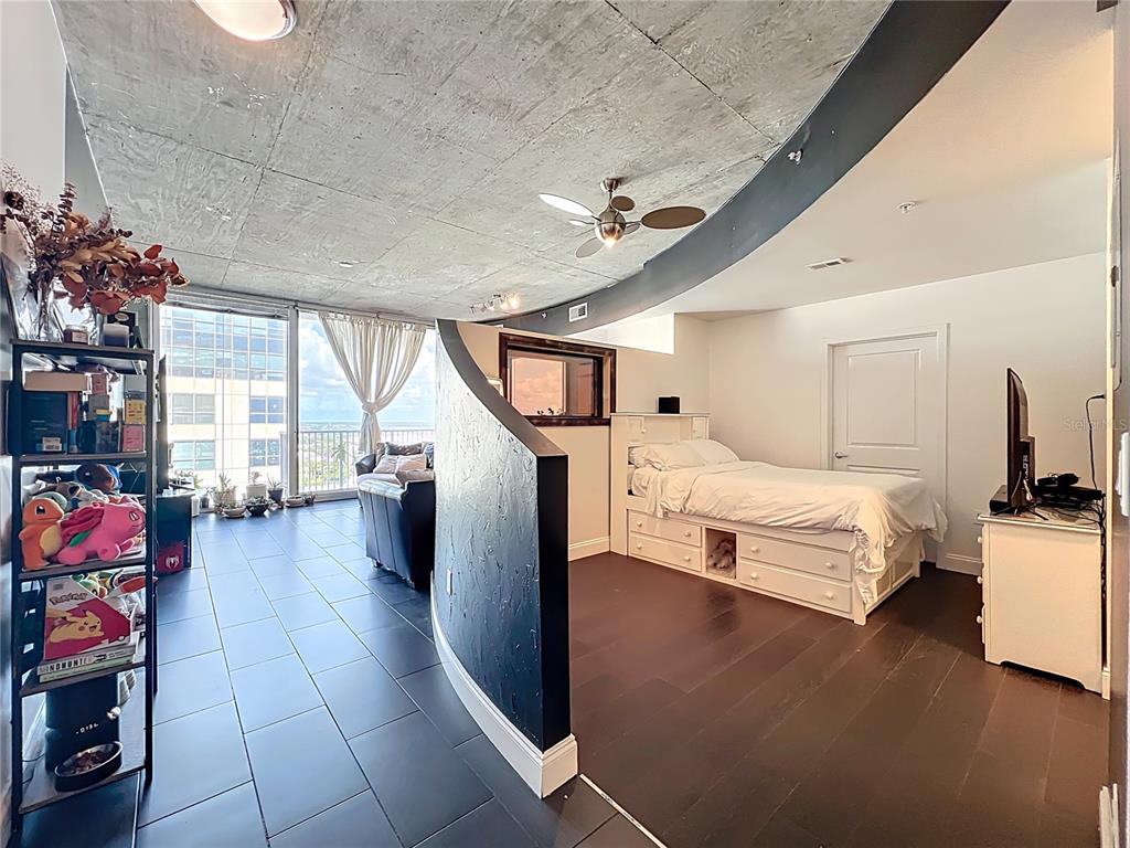 A studio apartment features a curved black partition, concrete ceiling, and a bed with storage — 155 S COURT AVENUE UNIT 1908, ORLANDO, FL