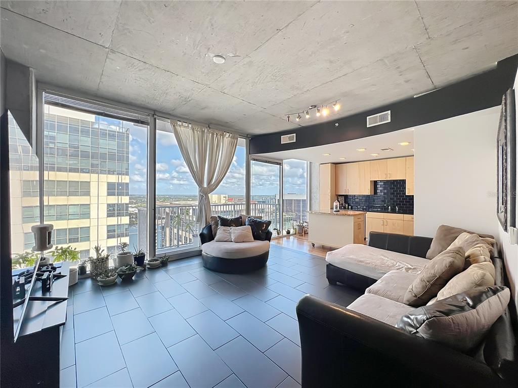 A modern living room with concrete ceilings, tile floors, and floor-to-ceiling windows overlooking a city — 155 S COURT AVENUE UNIT 1908, ORLANDO, FL
