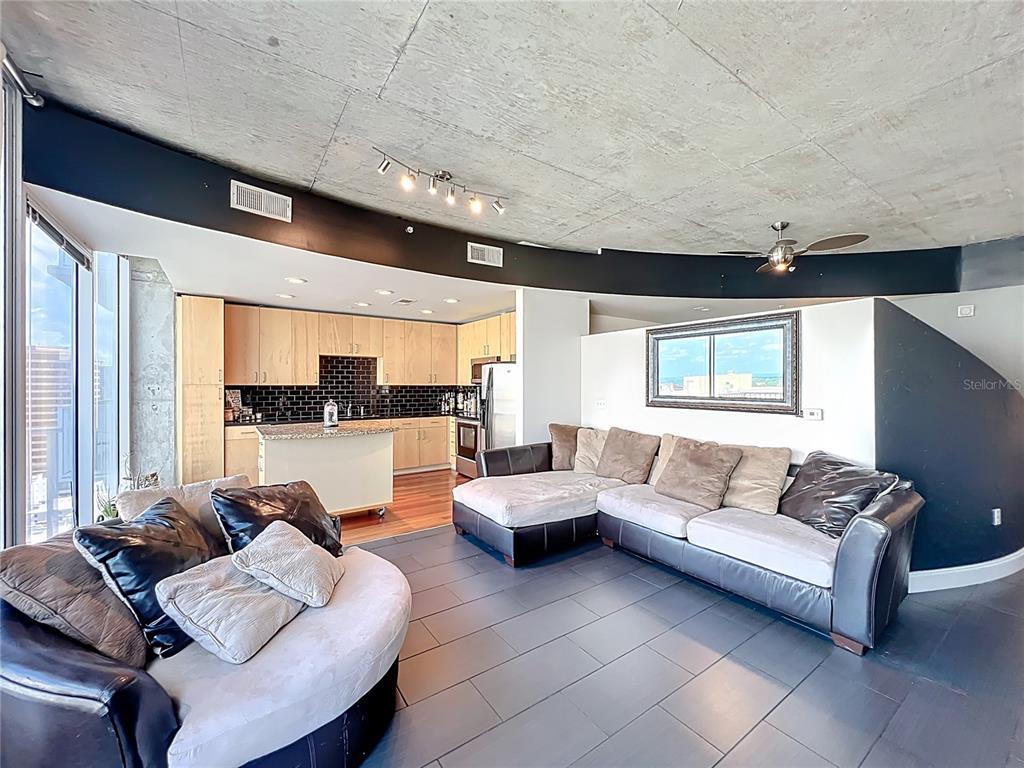 An open-concept living room and kitchen feature a concrete ceiling, tile flooring, and modern furniture — 155 S COURT AVENUE UNIT 1908, ORLANDO, FL
