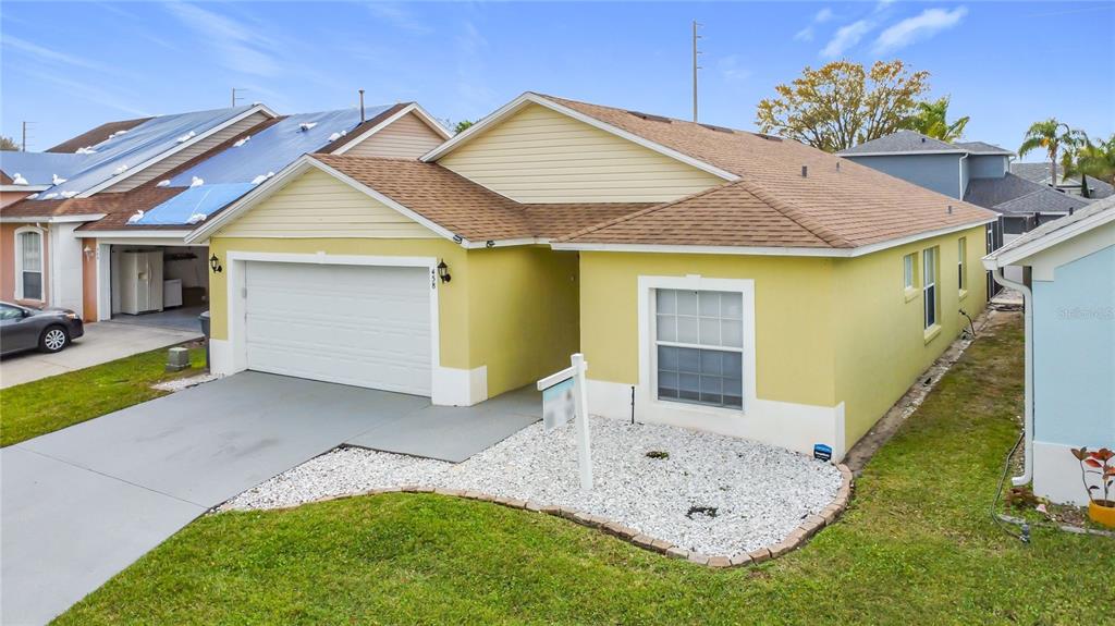 A yellow single-story house with a white garage door and a white rock front yard — 458 HOLLINGHEAD LOOP, DAVENPORT, FL