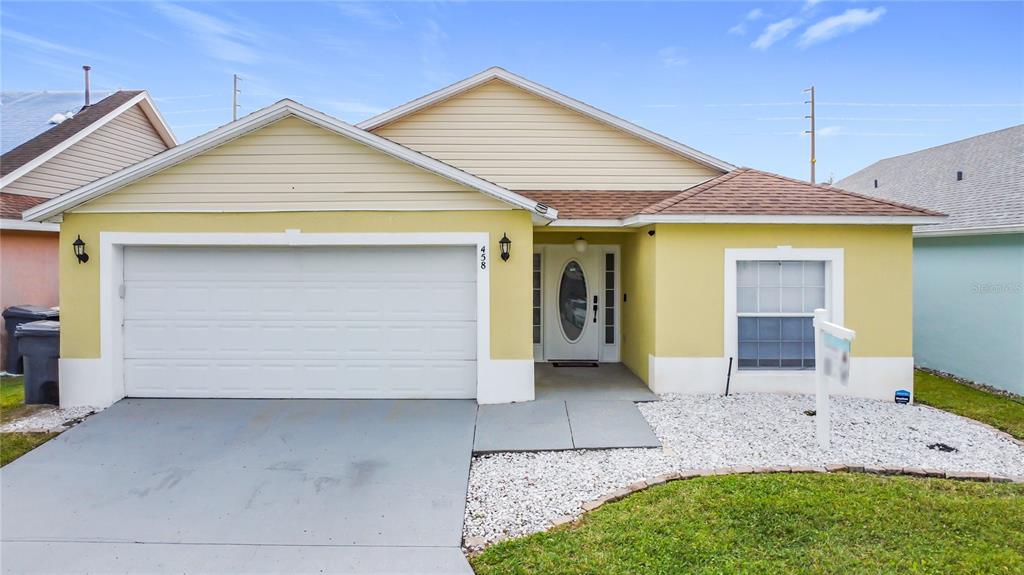 A single-story house with yellow stucco, a white garage door, and a white front door — 458 HOLLINGHEAD LOOP, DAVENPORT, FL