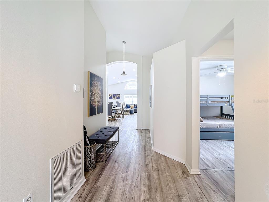 A hallway with wood-look flooring leads to a living area, with a bedroom visible on the right — 458 HOLLINGHEAD LOOP, DAVENPORT, FL