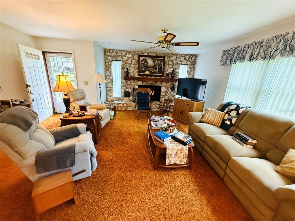 A living room features orange carpet, a stone fireplace, a ceiling fan, and comfortable seating — 7510 NW 128TH PLACE, ALACHUA, FL
