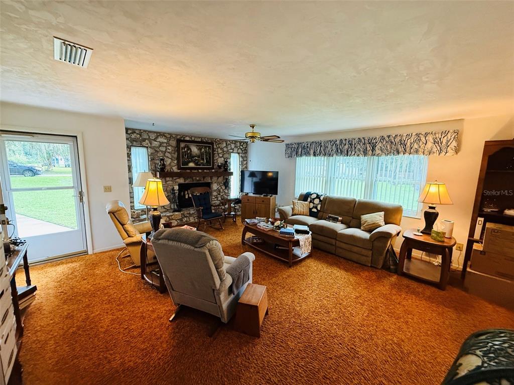 A living room features a stone fireplace, orange wall-to-wall carpeting, and a large window — 7510 NW 128TH PLACE, ALACHUA, FL