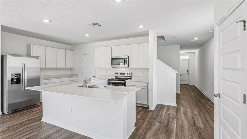 A modern kitchen features white cabinetry, stainless steel appliances, a center island, and wood-look flooring — 5588 TAVERNA LOOP, WINTER HAVEN, FL