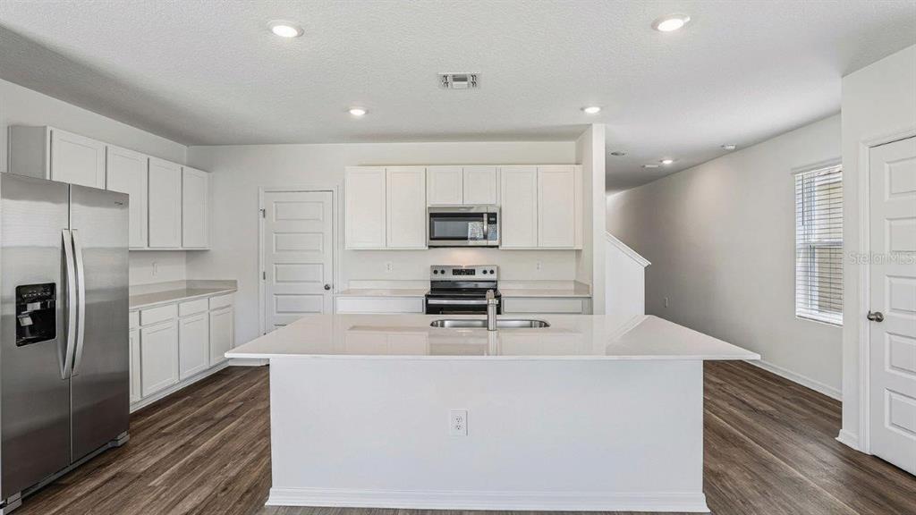 A modern kitchen features white cabinetry, stainless steel appliances, and a large central island — 5588 TAVERNA LOOP, WINTER HAVEN, FL