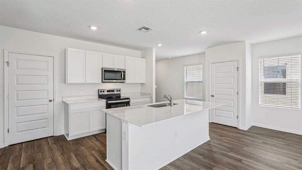 A modern kitchen features white cabinetry, stainless steel appliances, a center island, and wood-look flooring — 5588 TAVERNA LOOP, WINTER HAVEN, FL