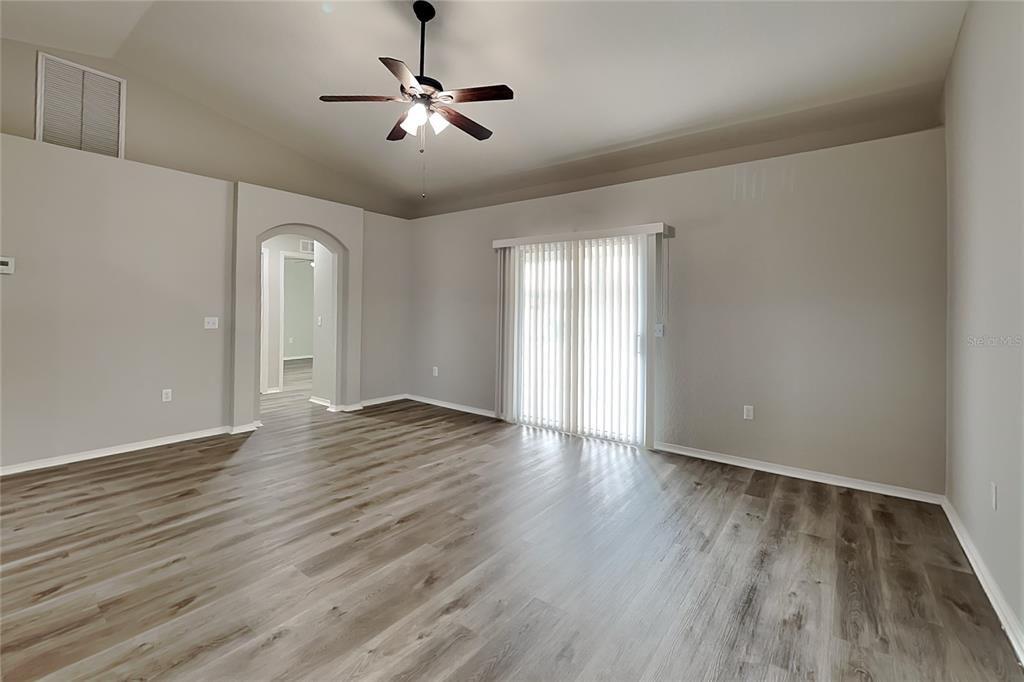 An empty living room with light gray walls, wood-look flooring, a ceiling fan, and sliding doors — 495 MAJESTIC GARDENS BOULEVARD, WINTER HAVEN, FL