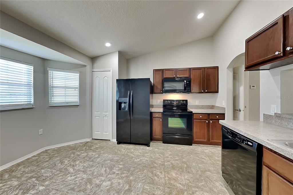 A kitchen features dark wood cabinets, black appliances, light countertops, and tile flooring — 495 MAJESTIC GARDENS BOULEVARD, WINTER HAVEN, FL
