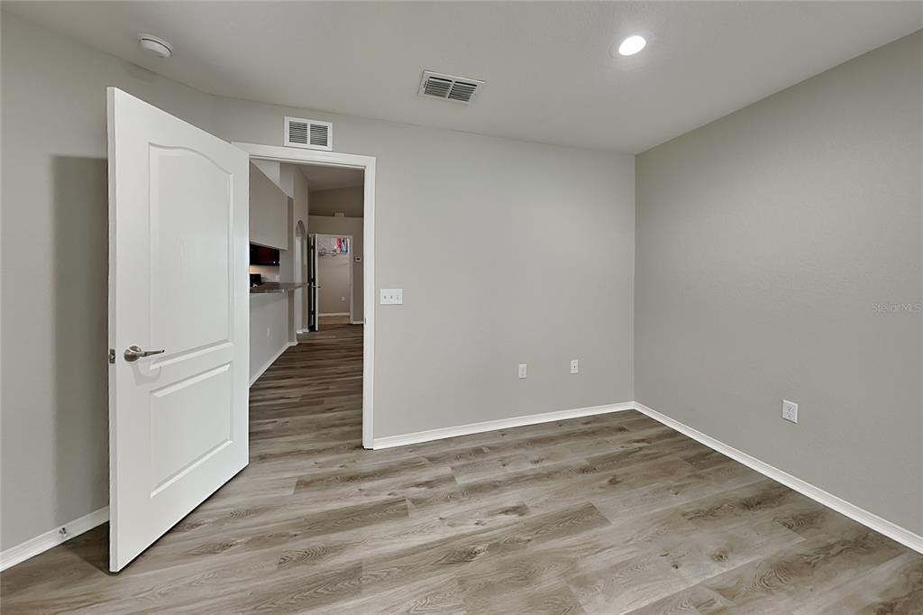 An empty room features light gray walls, wood-look flooring, and a white interior door — 495 MAJESTIC GARDENS BOULEVARD, WINTER HAVEN, FL