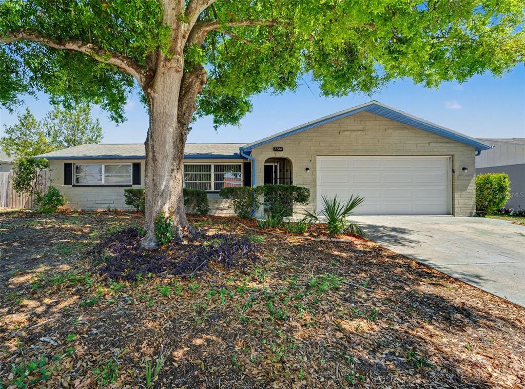 A single-story house with a brick facade, a two-car garage, and a large shade tree — 7744 WATERFORD STREET, NEW PORT RICHEY, FL